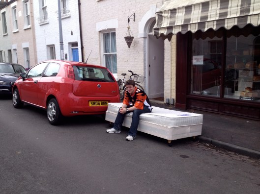 Why is this man sitting on a bed in the street?